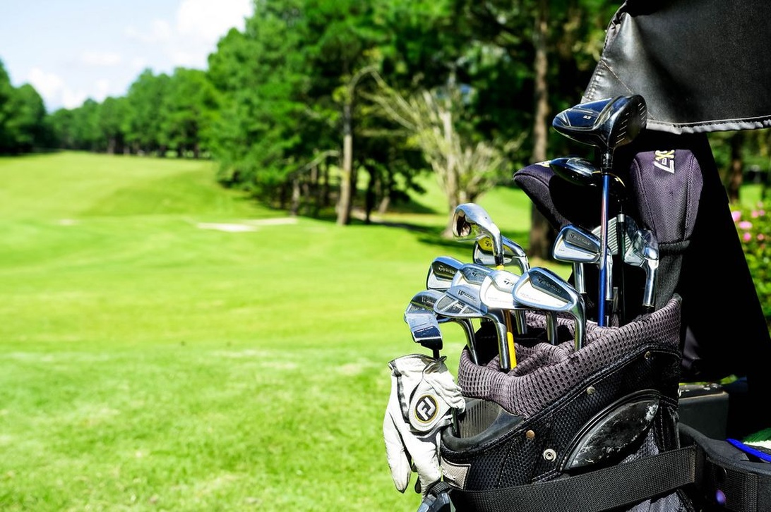 En närbild på en golfbag fylld med skinande golfklubbor på en grön golfbana.